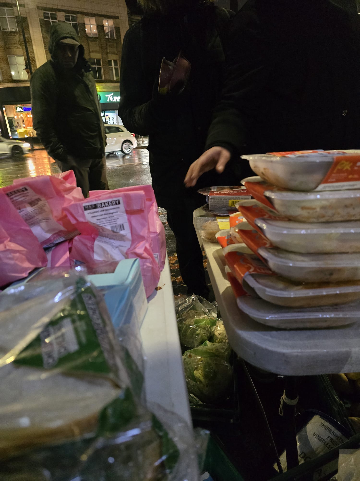 Volunteers serving prepared meals to community members on the street at night